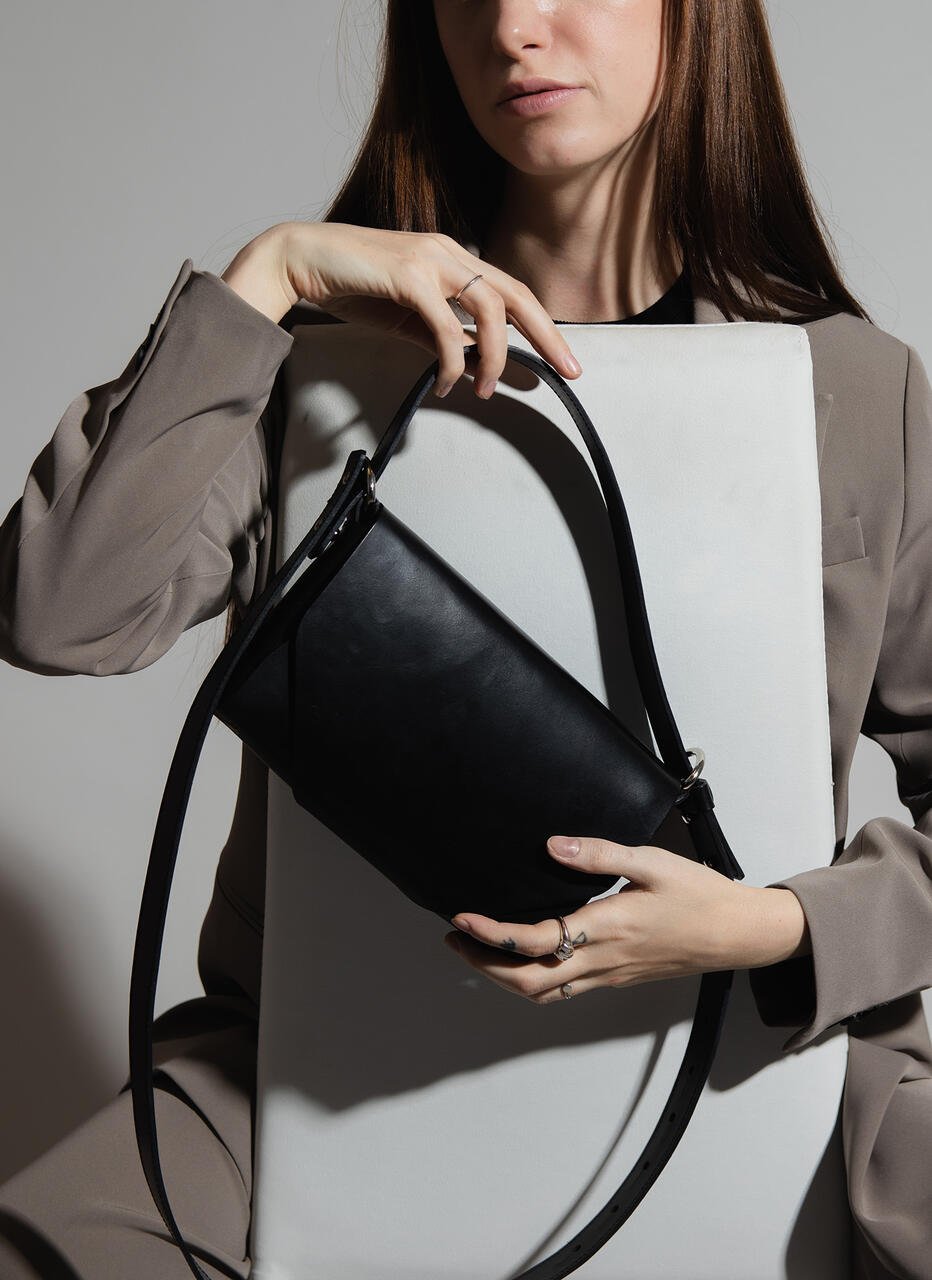 9. Woman posing with black leather Stella Soomlais shoulder bag against white panel, wearing grey suit
