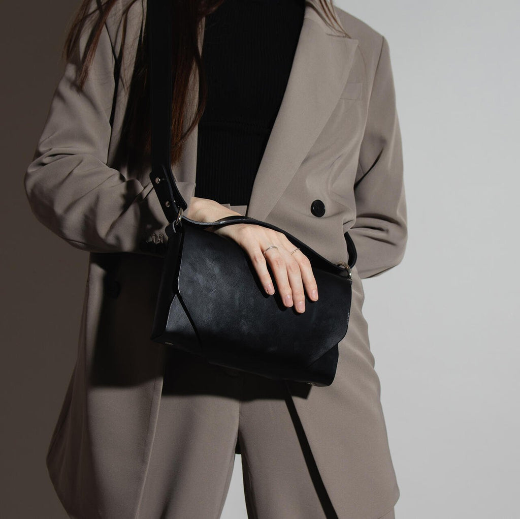 7. Woman holding black leather Stella Soomlais shoulder bag against grey suit in studio lighting
