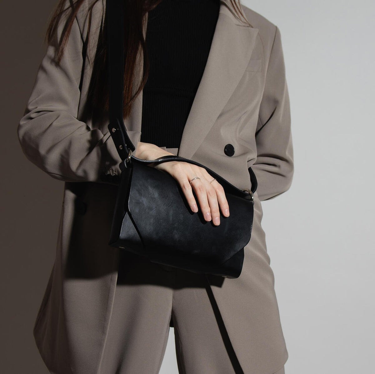 7. Woman holding black leather Stella Soomlais shoulder bag against grey suit in studio lighting