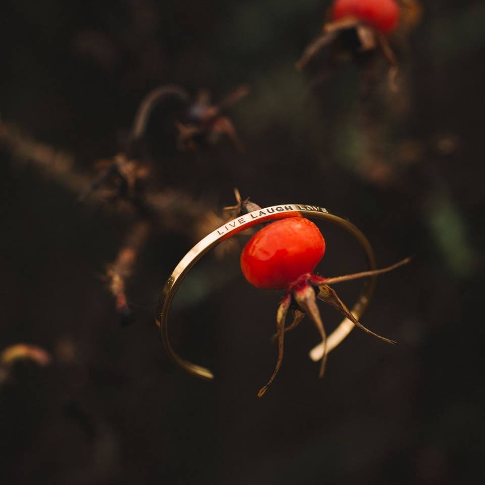 2. Olla's Live Laugh Love bracelet in gold, artistically displayed with a red berry in nature