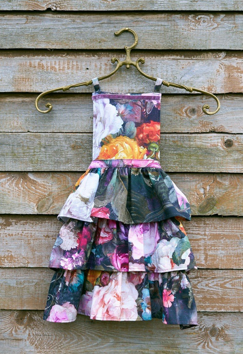 2. Hortensias Home Francine Black kids apron with dark floral print hanging on a wooden wall, showcasing layered design