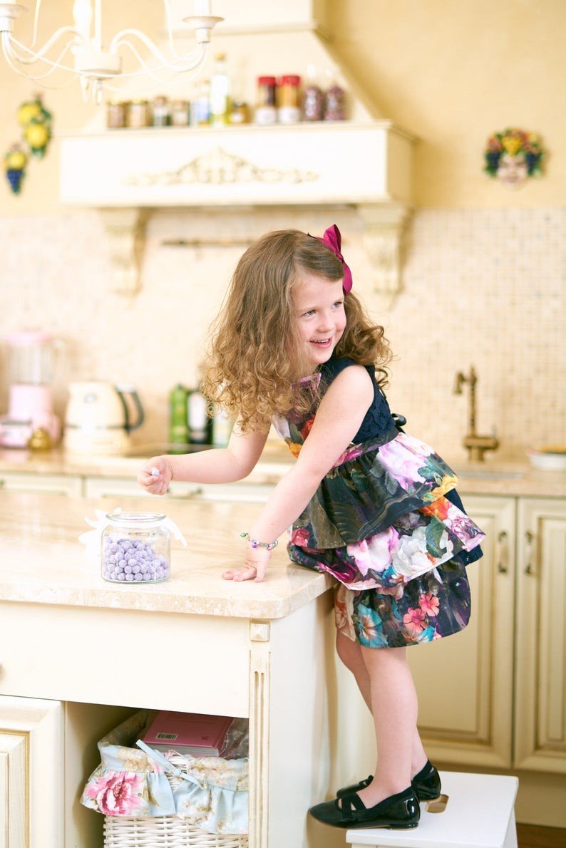 1. Young girl reaching for a jar on a kitchen counter wearing Hortensias Home Francine Black kids apron with dark floral print