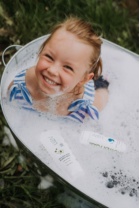 1. Smiling child in striped swimsuit enjoying bath with LUUV pear-scented bubbles in outdoor setting