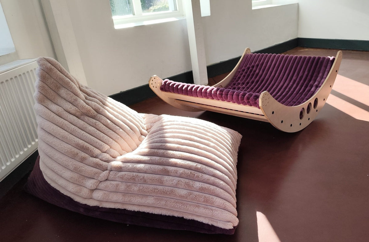 2. Luula kids bean bag chair in berry and rose mousse tones next to a wooden lounger, in a sunlit room with large windows