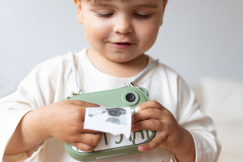 1. Child holding green Hoppstar camera, printing a black and white photo indoors