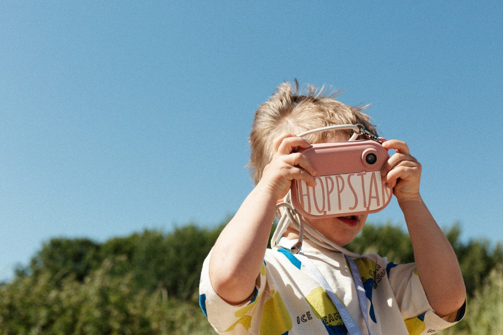 1. Child using pink Hoppstar camera outdoors with blue sky background