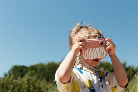 1. Child using pink Hoppstar camera outdoors with blue sky background
