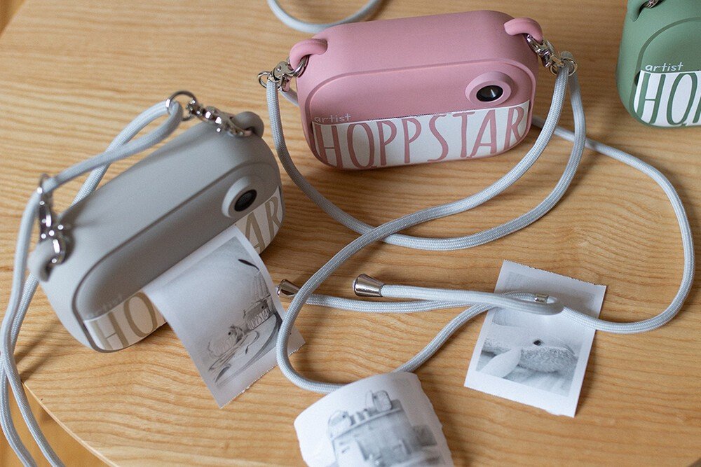 4. Flat lay of multiple Hoppstar cameras in various colors with printed photos on wooden surface