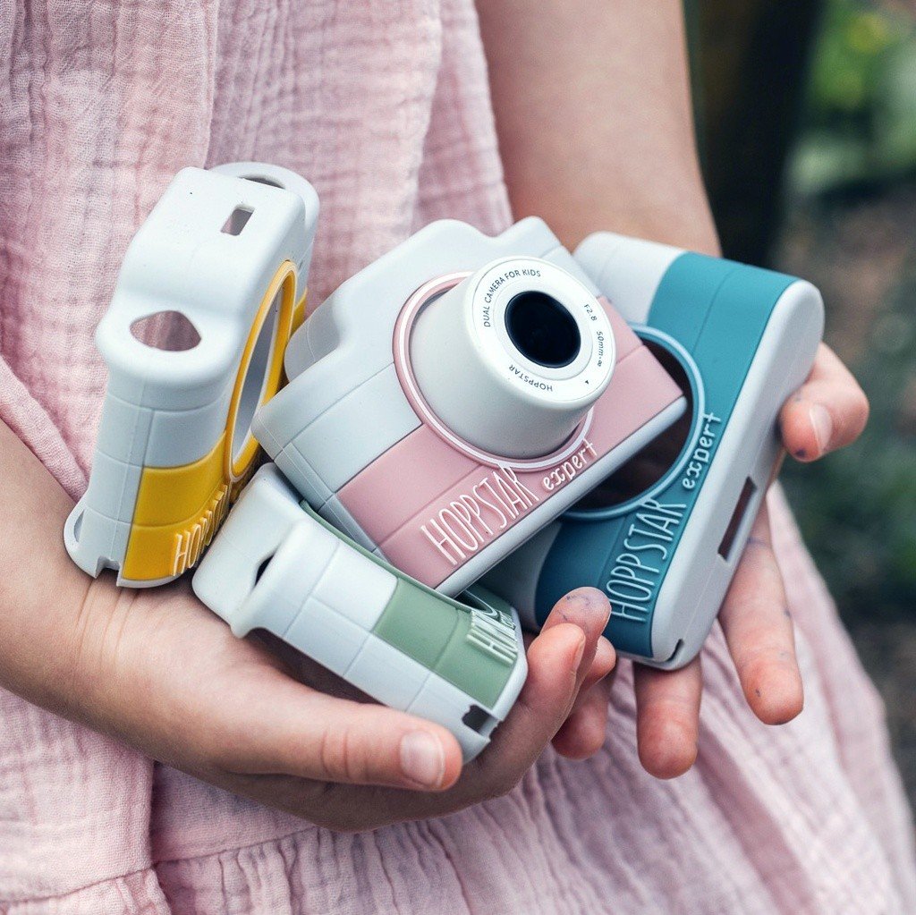 1. Child holding multiple Hoppstar Expert cameras in different colors, outdoors