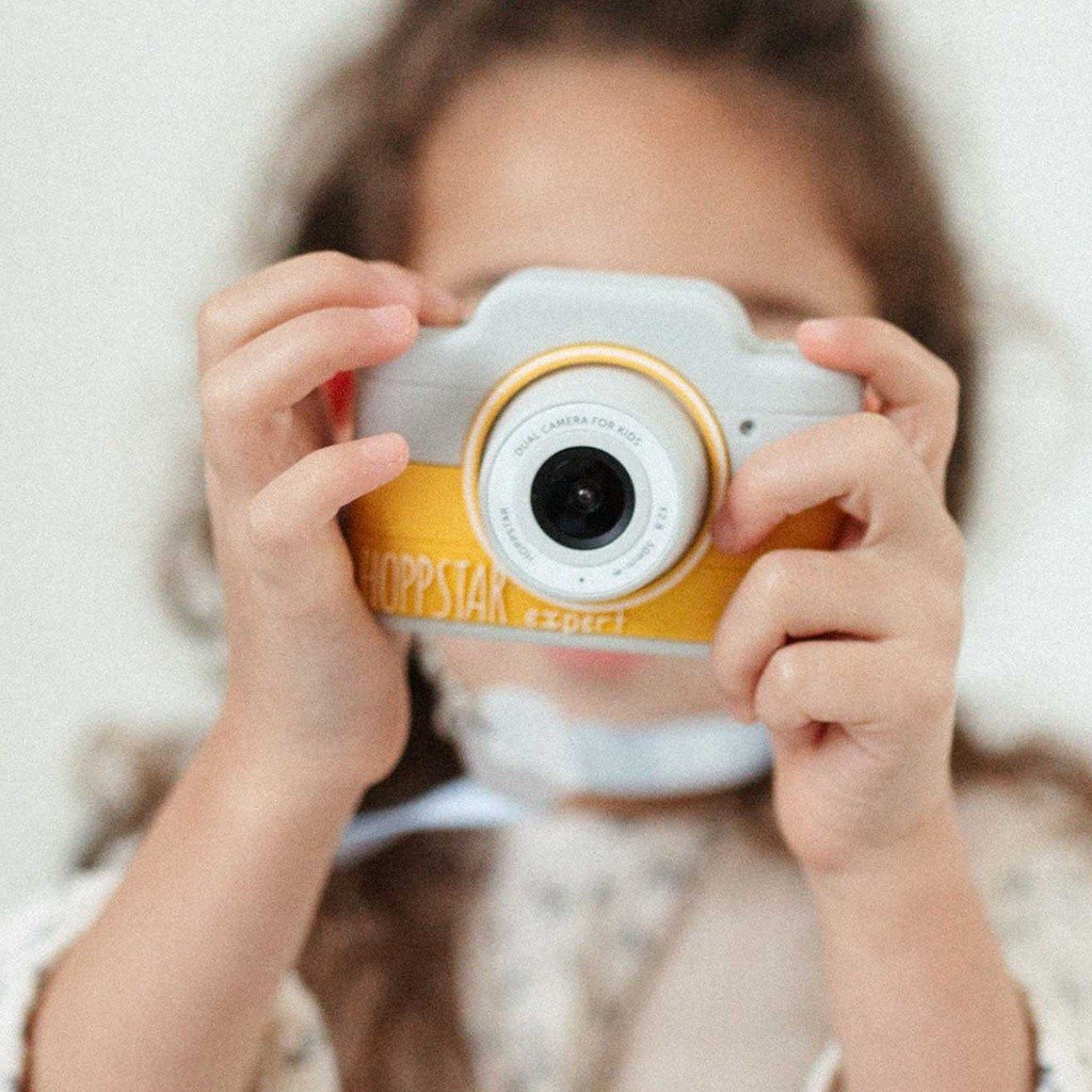 1. Child holding yellow Hoppstar Expert camera, partially visible face, indoors
