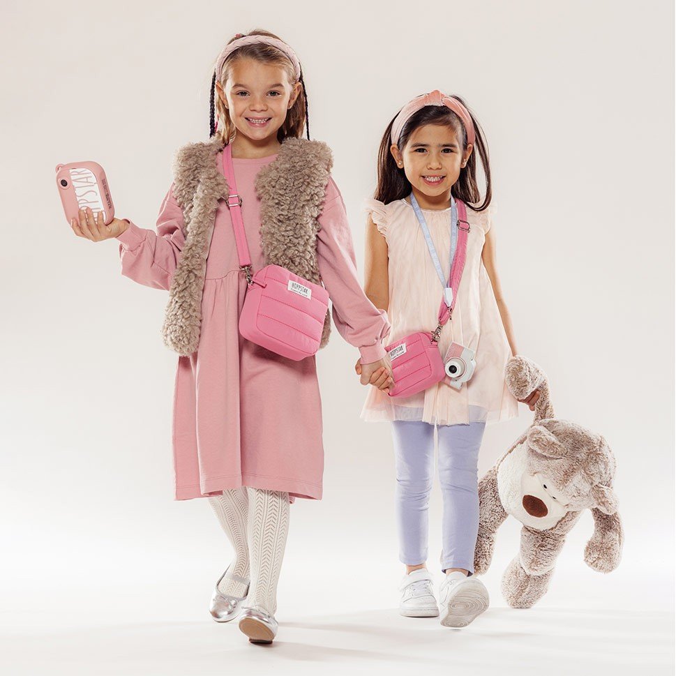 1. Two girls holding pink Hoppstar Expert cameras, wearing casual outfits in studio setting