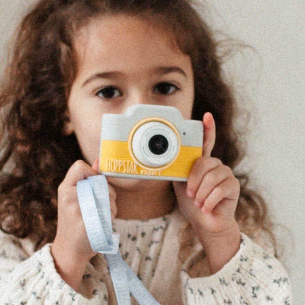 1. Child holding yellow Hoppstar Expert camera, smiling indoors