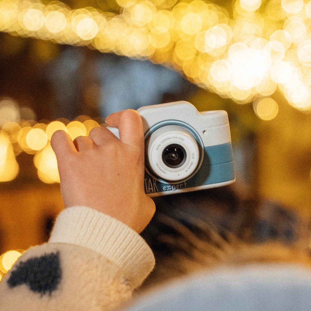 1. Child holding blue Hoppstar Expert camera with festive lights in background