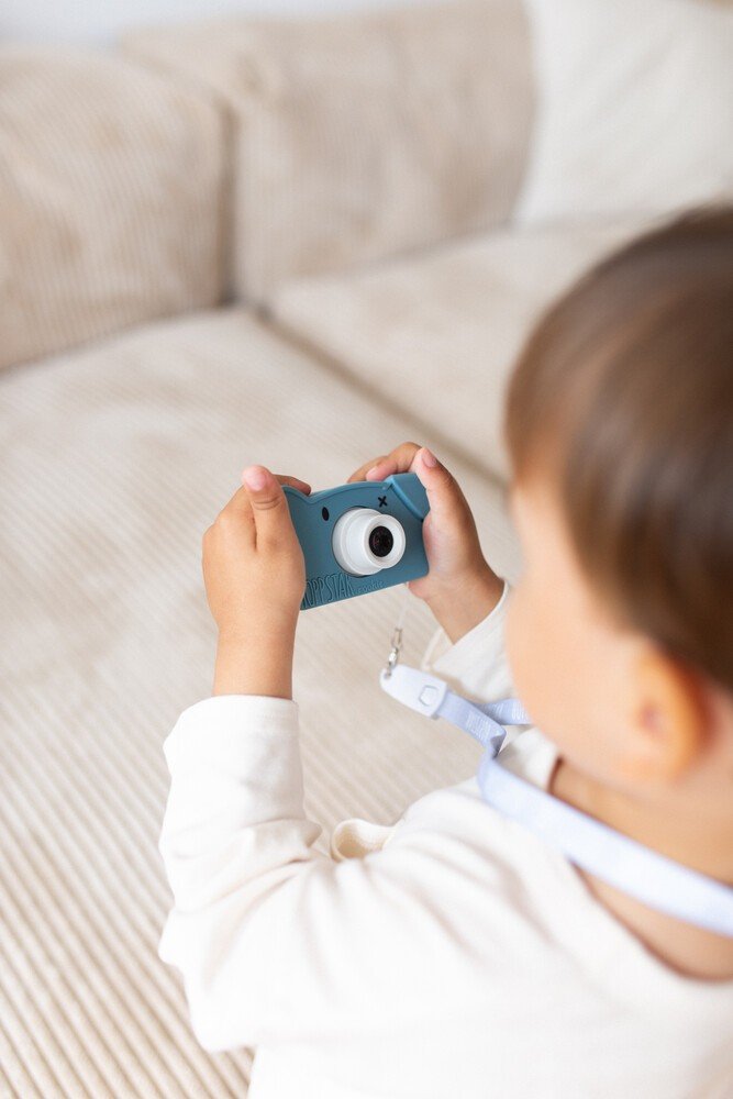 1. Child using blue Hoppstar Rookie camera indoors, focusing on screen