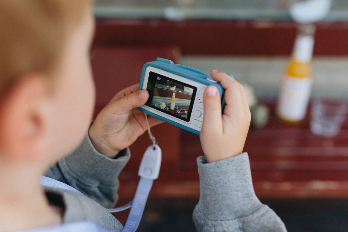 1. Child using blue Hoppstar Rookie camera, focusing on screen outdoors
