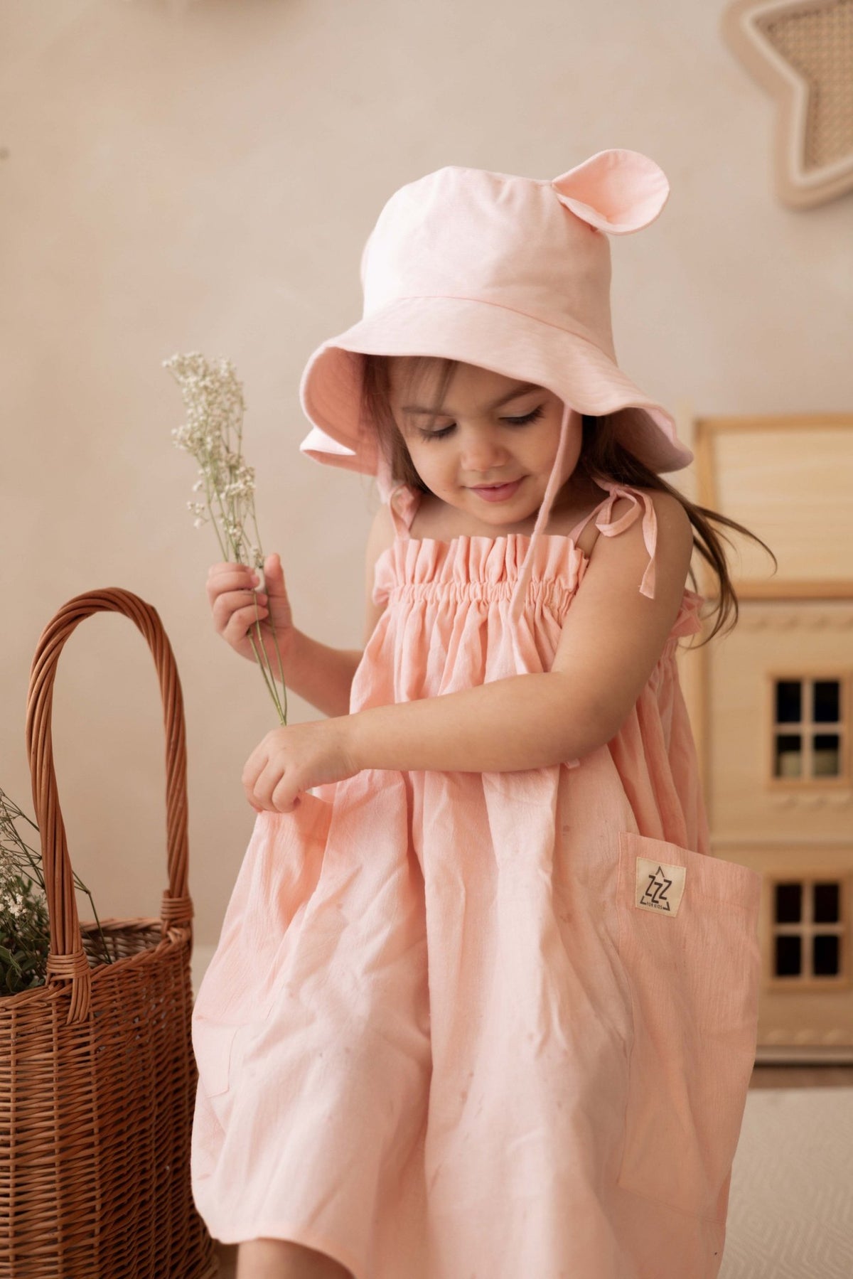 4. Girl in peach dress with pink hat looking down holding flowers indoors