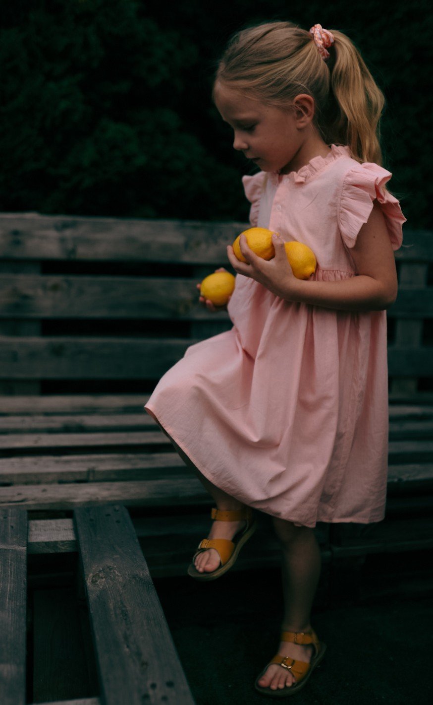 2. Girl in peach Zezuzulla dress with ruffled sleeves holding lemons, stepping on wooden bench