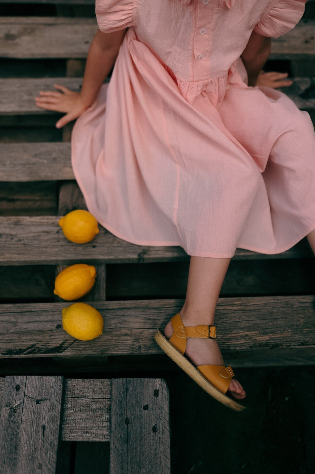 3. Close-up of girl sitting in peach Zezuzulla dress with lemons on wooden bench