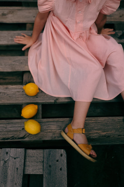 3. Close-up of girl sitting in peach Zezuzulla dress with lemons on wooden bench