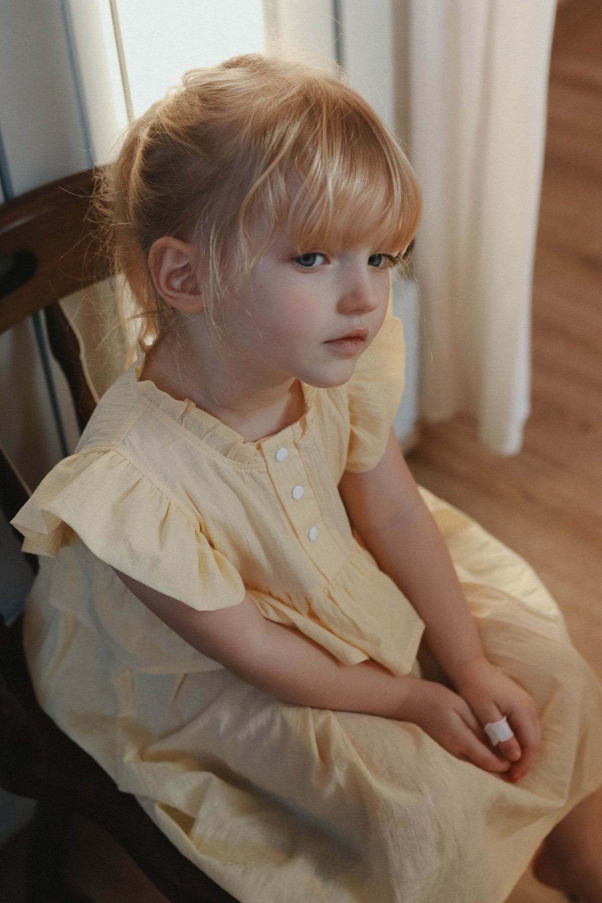 3. Close-up of young girl in yellow Zezuzulla dress with ruffled sleeves sitting indoors