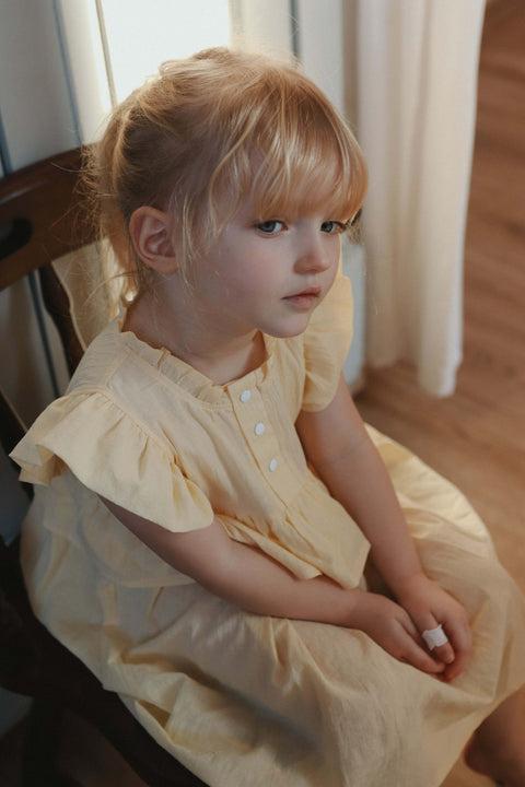 3. Close-up of young girl in yellow Zezuzulla dress with ruffled sleeves sitting indoors