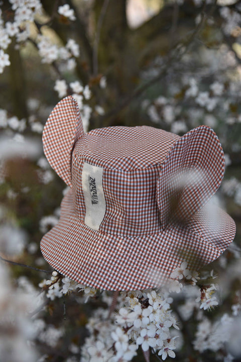 1. Zezuzulla kids chequered hat with fabric ears and brand label, placed among blooming branches in a natural setting