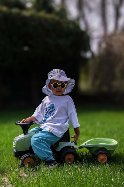 2. Child on toy tractor wearing Zezuzulla striped bucket hat with fabric ears, in a garden