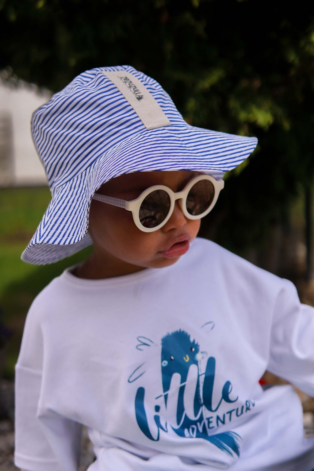 1. Child wearing Zezuzulla striped bucket hat with fabric ears and sunglasses, outdoors