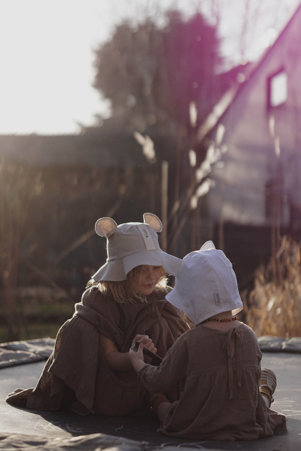 4. Two children sitting on trampoline wearing beige and white hats with ears