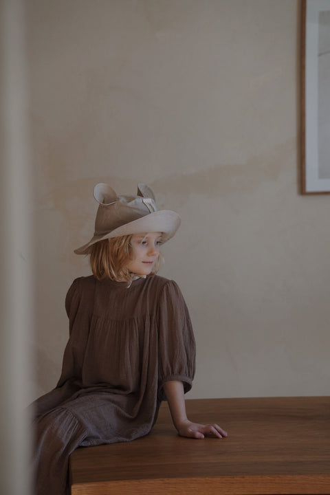 5. Child sitting indoors wearing beige hat with ears and brown dress