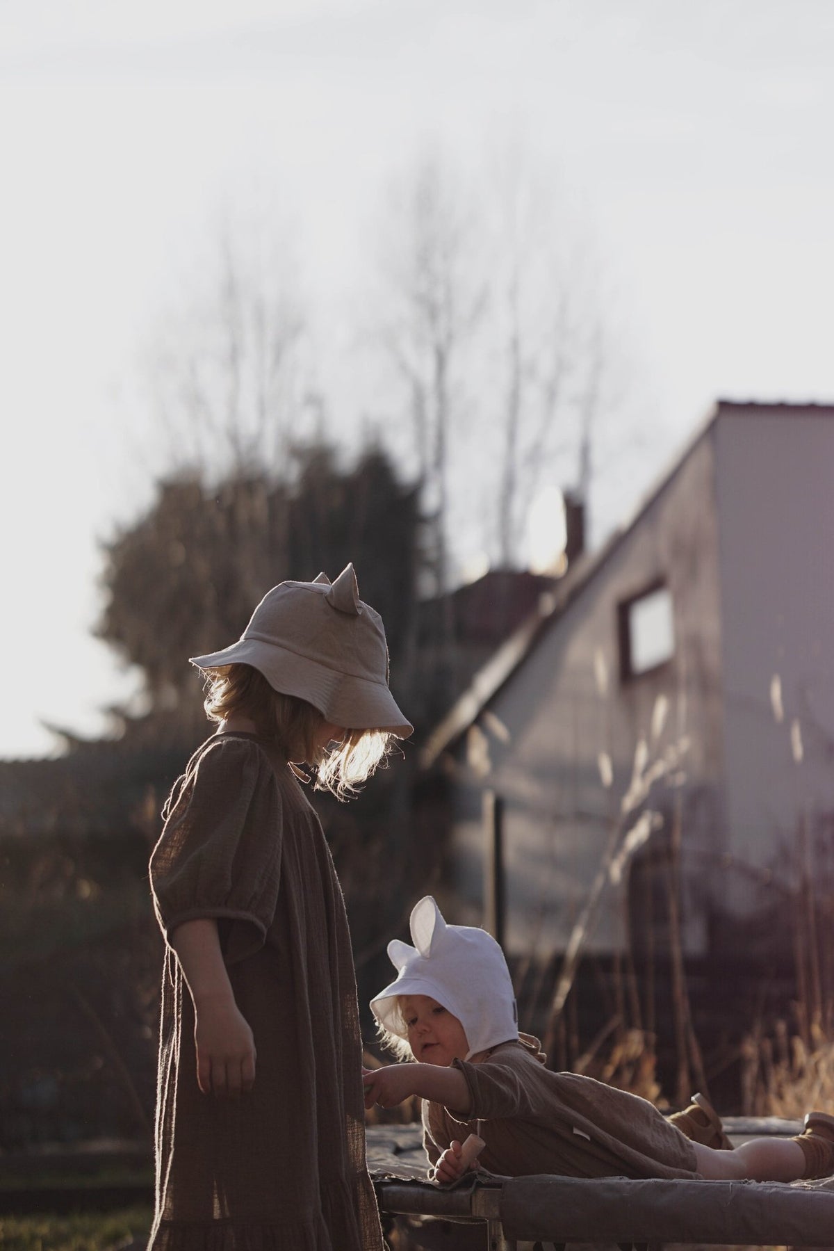 3. Two children wearing beige and white hats with ears playing outdoors