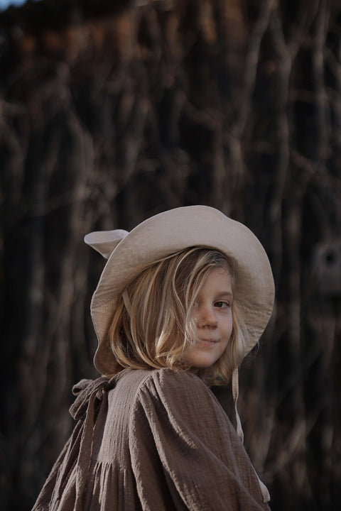 1. Child wearing beige kids hat with ears and brown dress in outdoor setting