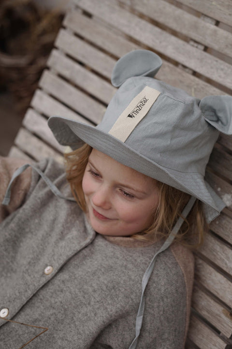 1. Child lying on wooden bench wearing grey hat with ears, looking relaxed