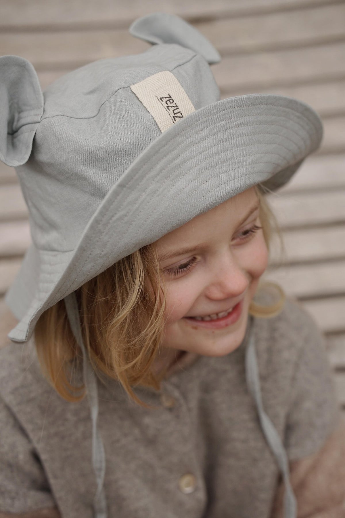 1. Child wearing grey hat with ears and smiling, sitting on wooden bench outdoors