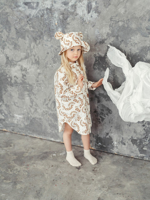 2. Child wearing Zezuzulla kids hat with ears and matching dress, standing against a textured grey wall
