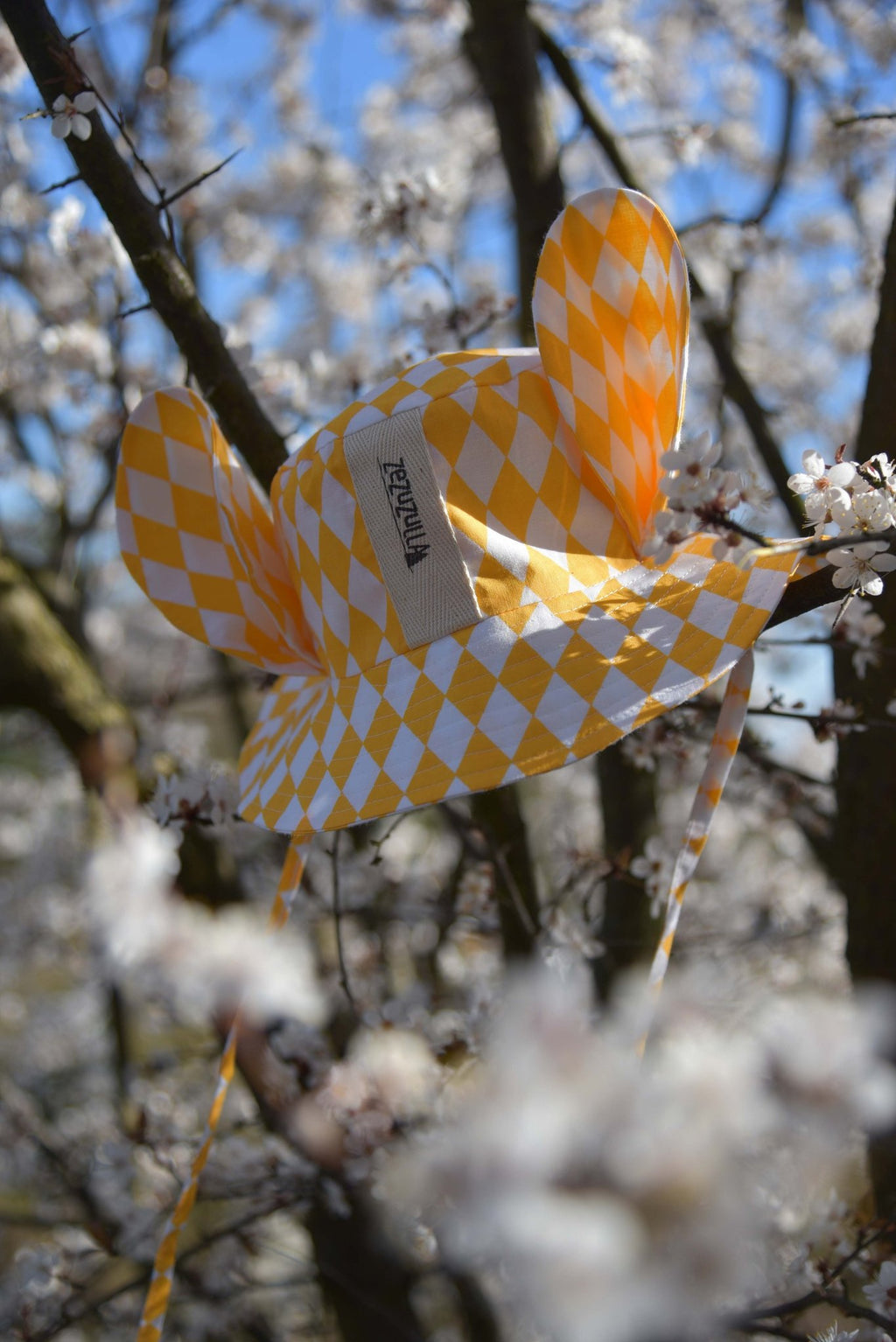 3. Close-up of yellow and white checkered hat with ears on a blossoming tree branch