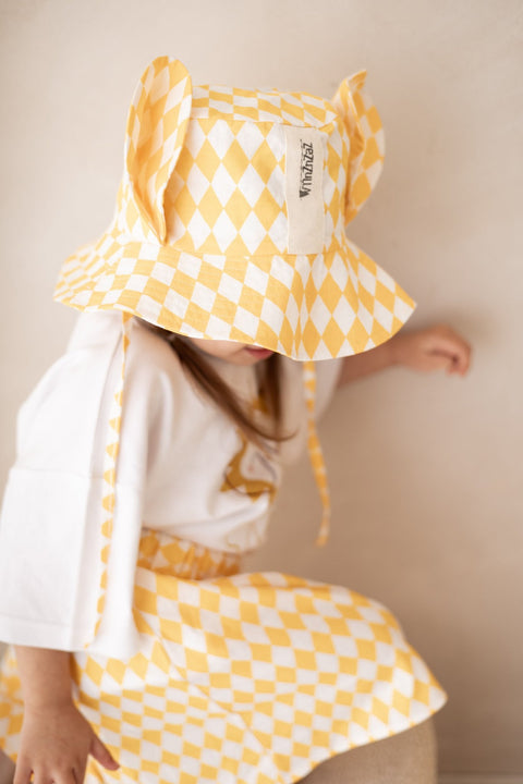 1. Child wearing yellow and white checkered hat with ears and matching skirt, sitting against a neutral background