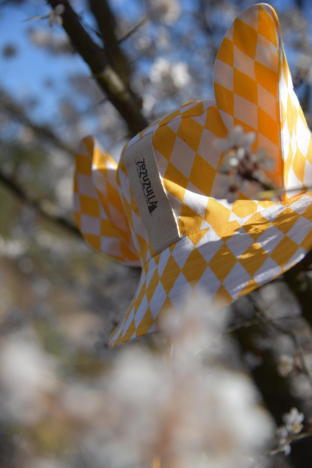 2. Yellow and white checkered hat with ears hanging on a tree branch with blossoms