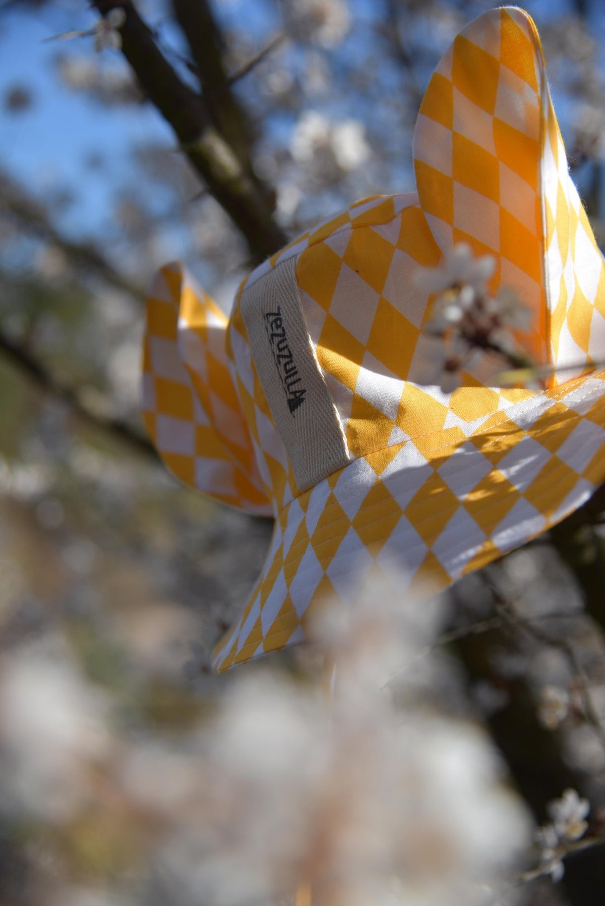2. Yellow and white checkered hat with ears hanging on a tree branch with blossoms