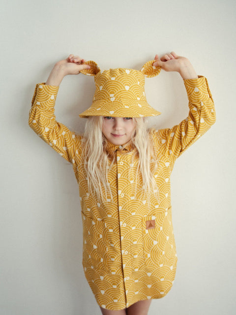 3. Child playfully holding ears of mustard hat with wave pattern, wearing matching outfit
