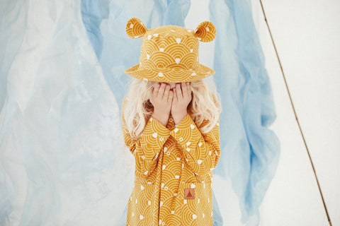 1. Child wearing mustard hat with ears and matching outfit, standing in front of blue fabric backdrop