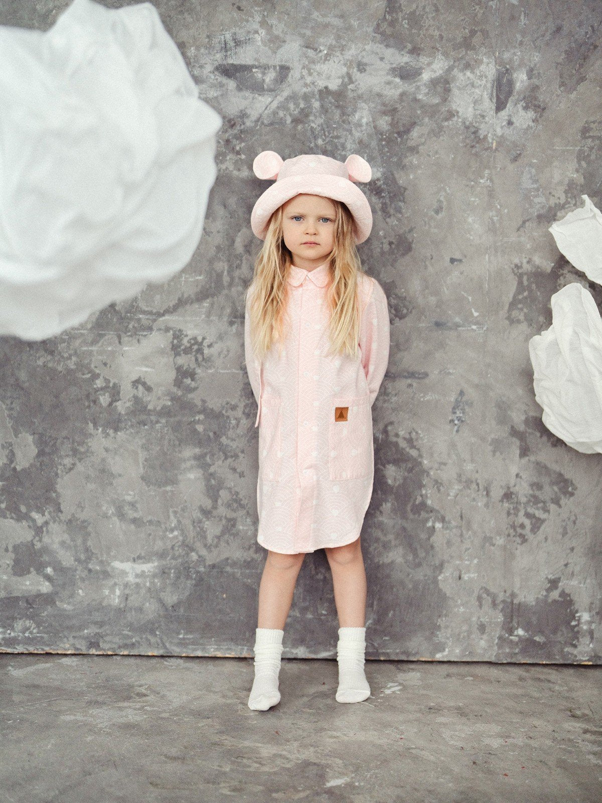 2. Full view of child in pink hat with ears and matching outfit, standing in artistic setting