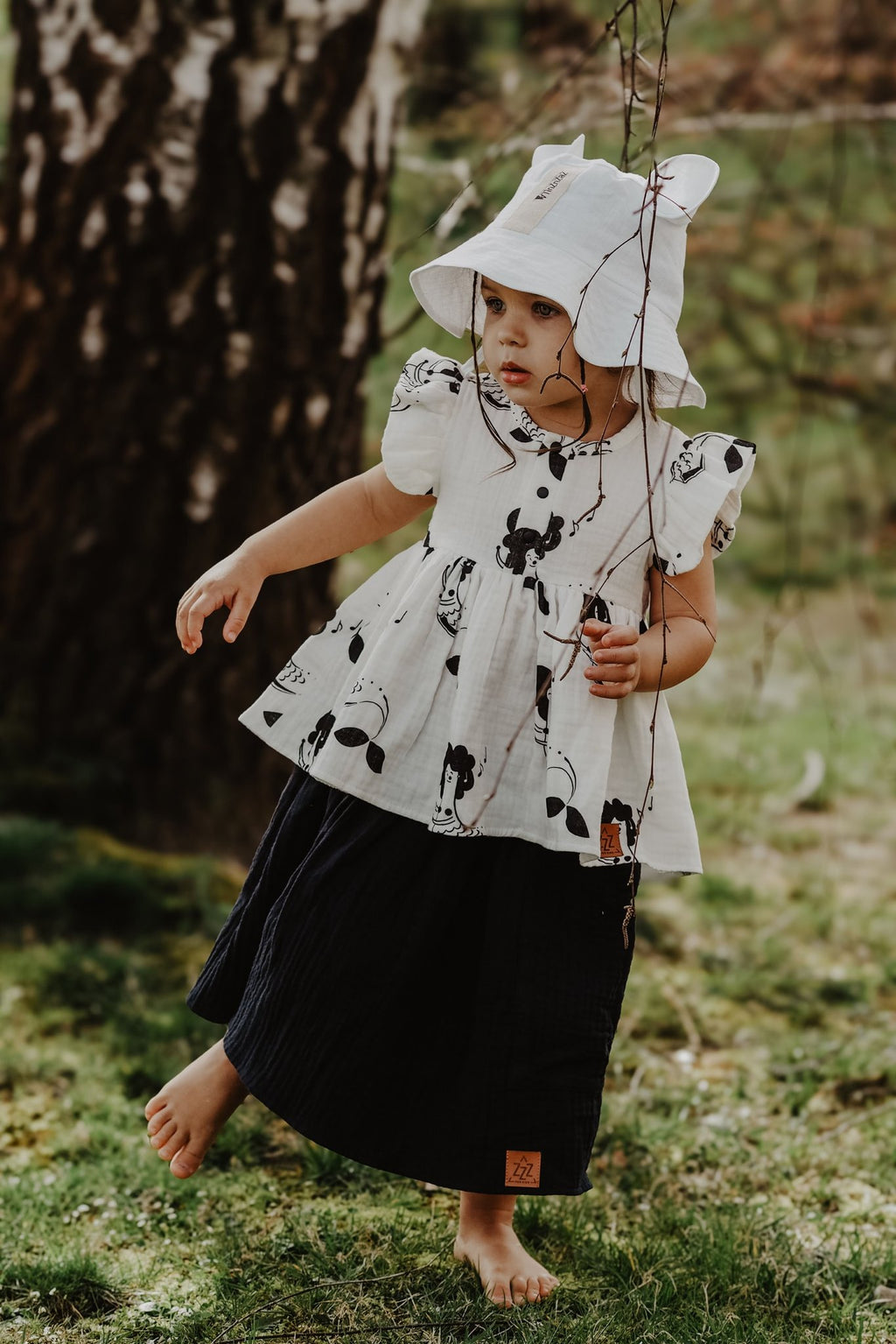 5. Child wearing white hat with ears and printed dress, playing outdoors