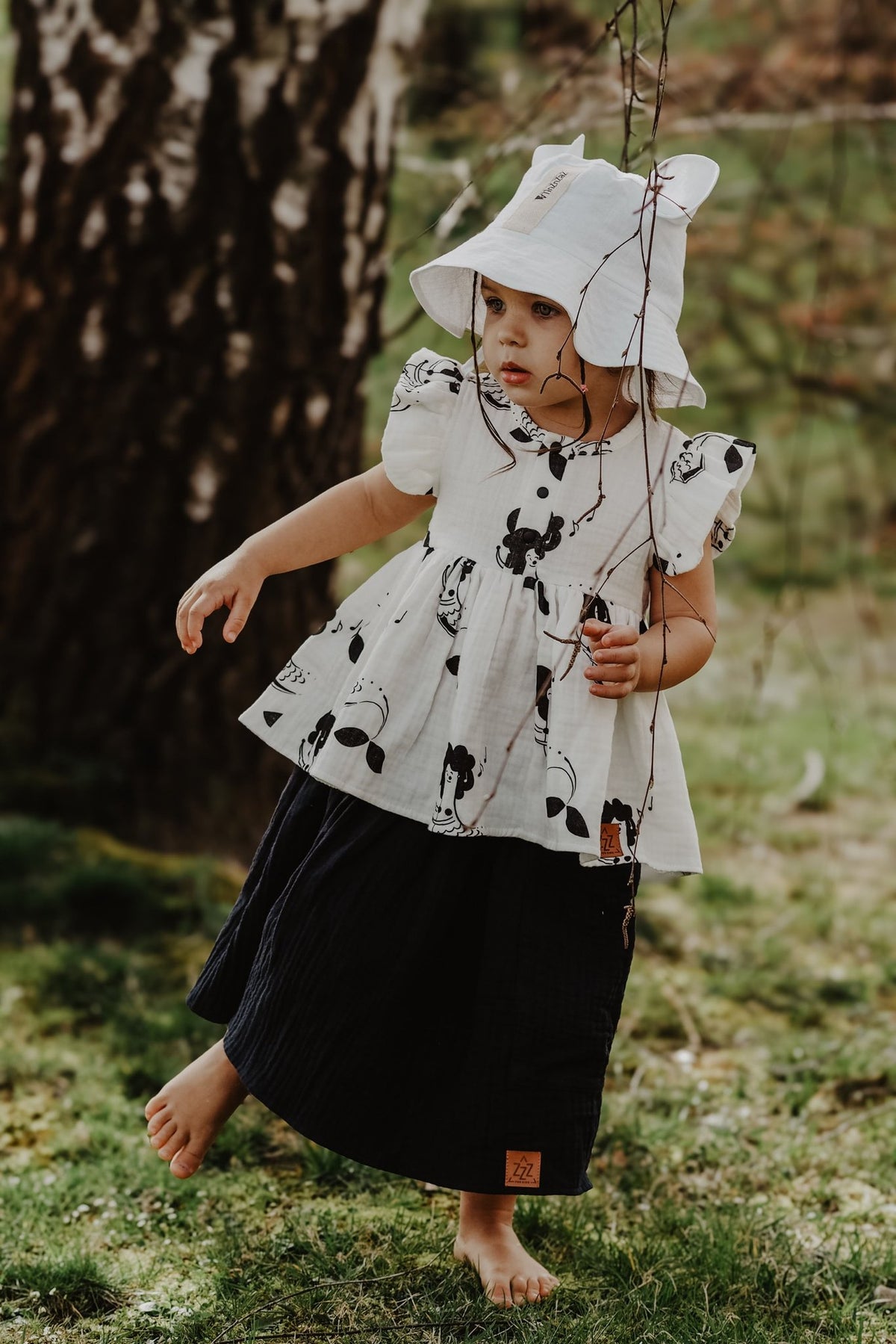 5. Child wearing white hat with ears and printed dress, playing outdoors