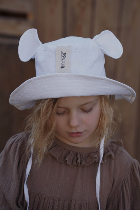 1. Child wearing white hat with ears and brown dress, looking down in outdoor setting