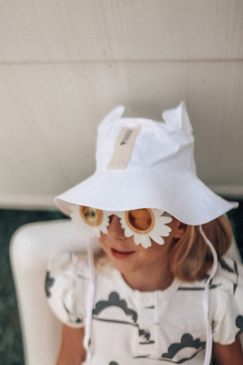 3. Child wearing white hat with ears and daisy sunglasses, sitting indoors