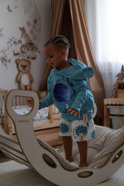 1. Child wearing blue hoodie with ears and moon print, standing on indoor play equipment in a cozy room