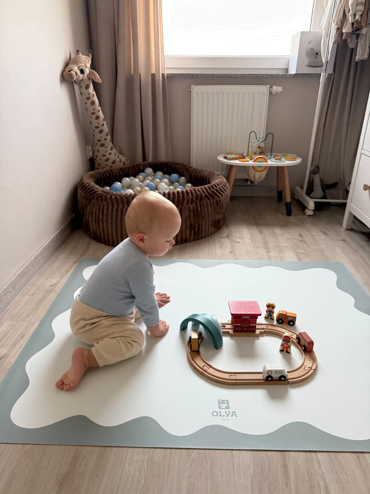 1. Baby playing on OLYA KIDS blue frame floor mat with toy train set in cozy nursery