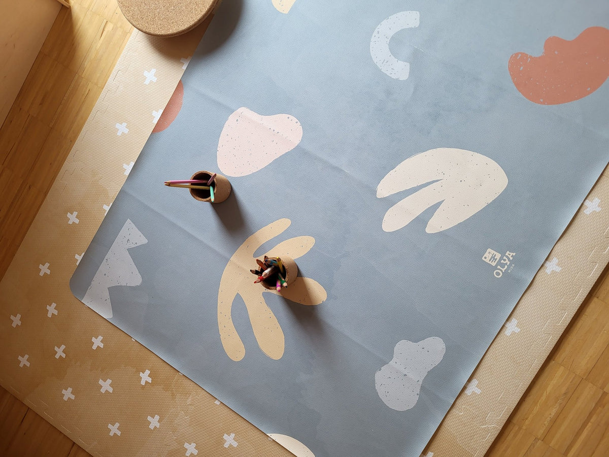 1. Kids' mealtime floor mat in organic sea design with abstract shapes, placed on wooden floor with two cups holding colored pencils
