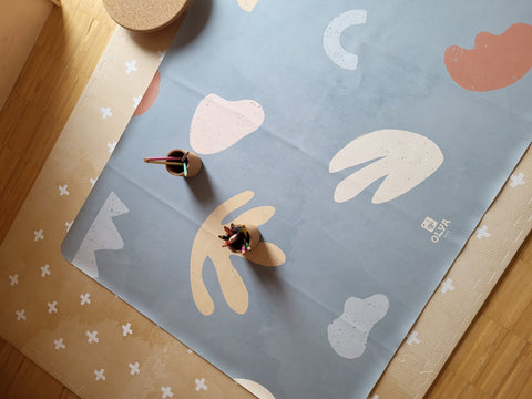 1. Kids' mealtime floor mat in organic sea design with abstract shapes, placed on wooden floor with two cups holding colored pencils